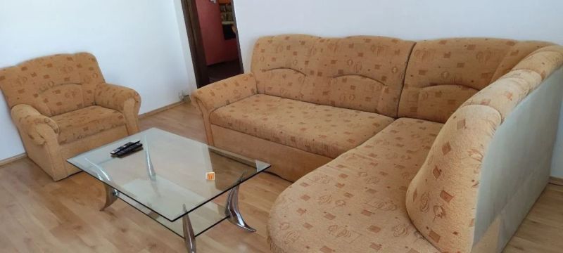 Prenájom 2 izbový byt Poprad - loggia - Obývačka v 2-izbovom byte s oranžovou sedacou súpravou, sklom stolom a podlahou s dreveným dekorom.