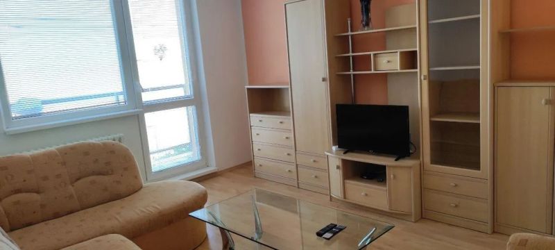 Prenájom 2 izbový byt Poprad - loggia - Obývacia izba v 2-izbovom byte s nábytkom a televízorom, podlaha s dreveným dekorom.