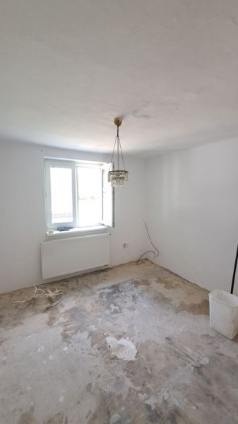 Pokojné bývanie v obci Kava + investícia do budúcnosti - Izba s lustrom a prázdnou podlahou na renováciu v rodinnom dome.