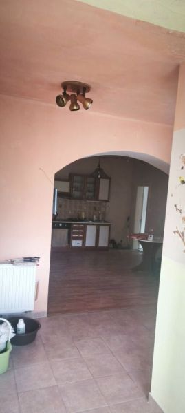 Pokojné bývanie v obci Kava + investícia do budúcnosti - Interiér rodinného domu s podlahou s dreveným dekorom a oblúkovým prechodom do kuchyne.