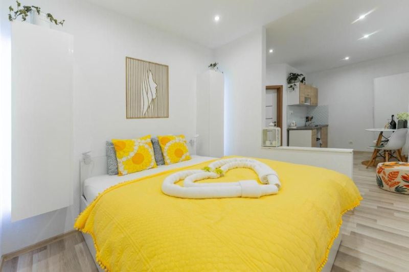 Moderný apartmán v centre Rajeckých Teplíc rovno oproti kúpeľom Afrodi - Rekreačný apartmán s posteľou, žltým prehozom a kuchynkou; podlaha s dreveným dekorom.