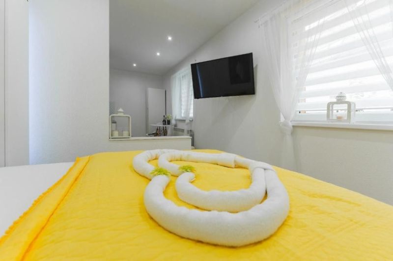Moderný apartmán v centre Rajeckých Teplíc rovno oproti kúpeľom Afrodi - Svetlá izba Rekreačného apartmánu s televízorom, žltou posteľnou bielizňou a dekoráciou z uterákov.