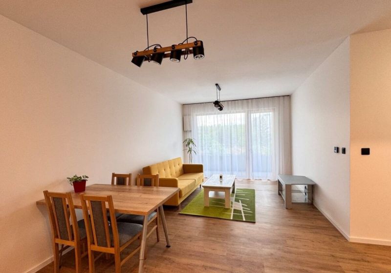 Prenájom nový 2-izbový byt -49m² Žilina-Vlčince, EUROTERRACE - Obývačka v 2-izbovom byte s pohovkou, podlahou s dreveným dekorom a jedálenským stolom.