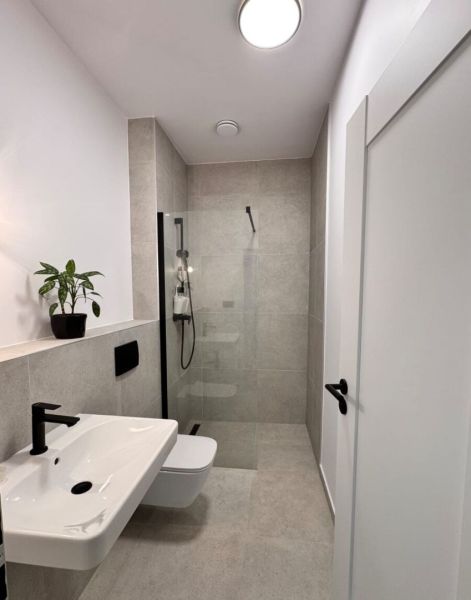 Prenájom nový 2-izbový byt -49m² Žilina-Vlčince, EUROTERRACE - Kúpeľňa v 2-izbovom byte s bielym umývadlom, sprchou a kvetináčom na poličke.