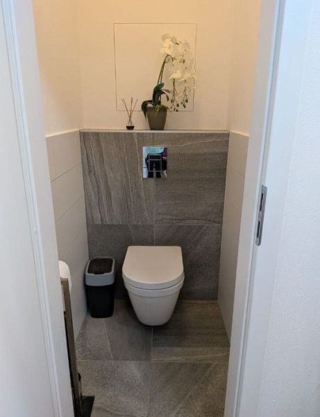 Moderný 2-izbový byt s balkónom a výhľadom - Toaleta v 2-izbovom byte s šedým obkladom a rastlinou na poličke.