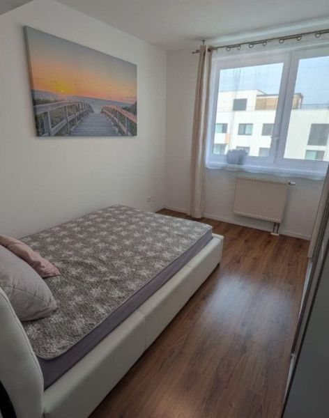 Moderný 2-izbový byt s balkónom a výhľadom - Spálňa v 2-izbovom byte s posteľou, obrazom a podlahou s dreveným dekorom.