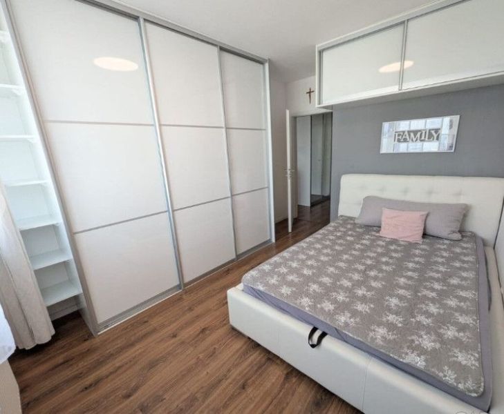 Moderný 2-izbový byt s balkónom a výhľadom - Spálňa v 2-izbovom byte s podlahou s dreveným dekorom, skriňou a posteľou.