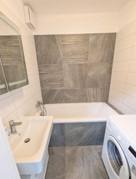 Moderný 2-izbový byt s balkónom a výhľadom - Kúpeľňa s umývadlom, vaňou a práčkou v 2-izbovom byte, obklady v šedom dekore.
