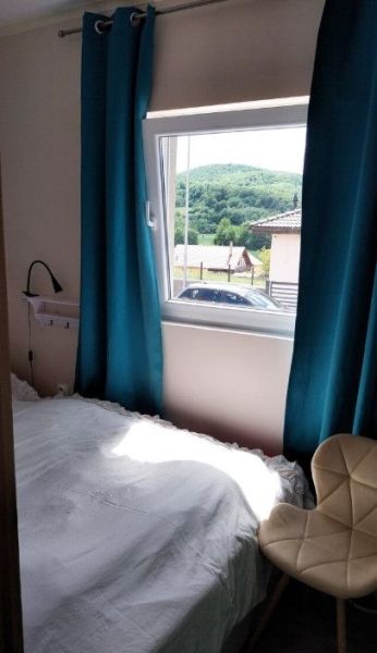 Mobilný celoročný drevodom – novostavba - Spálňa s jednoduchou posteľou, tyrkysovými závesmi a výhľadom na prírodu, Zvláštne nehnuteľnosti.
