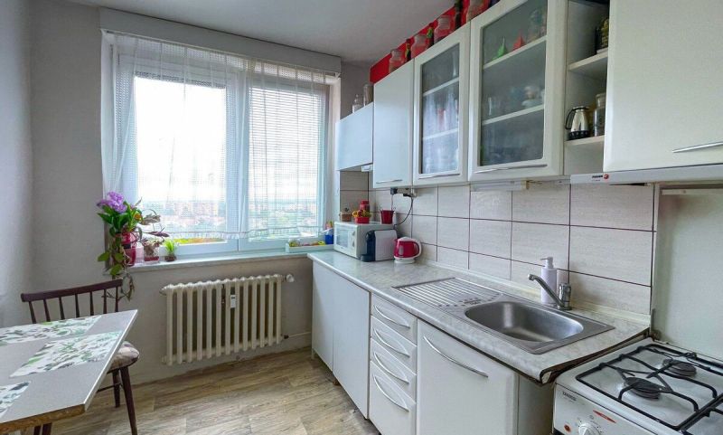 Predaj: Priestranný 3-izbový Byt s Balkónom a Potenciálom na Východe! - Kuchyňa v 3-izbovom byte s bielymi skrinkami a podlahou s dreveným dekorom.