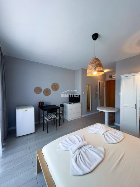 Moderná garsónka (41 m²) s výhľadom na bazén – Rezort ANTARES - Garsónka s posteľou, pracovným stolom, skriňou, mini chladničkou a podlahou s dreveným dekorom.
