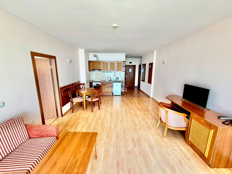 3-izbový apartmán v prvej línii pri mori s Aktom 16 - Obývacia izba v 3-izbovom byte s podlahou s dreveným dekorom a jednoduchým zariadením.