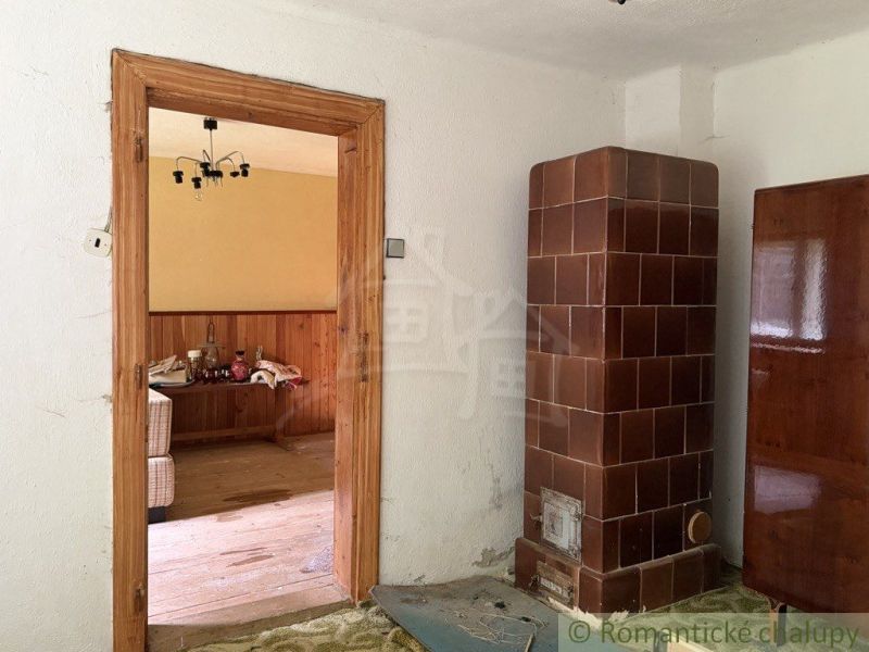 Chata na rekonštrukciu v lokalite Ružín - Bradan - Chata s kachľovou pecou, dreveným stolom a podlahou s dreveným dekorom.