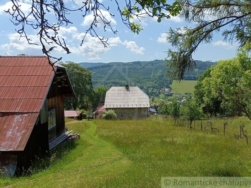 Pozemok s drevenicou na Kysuciach s krásnym výhľadom, Olešná - Exteriér chaty v Olešnej s výhľadom na zelené kopce a dedinu.