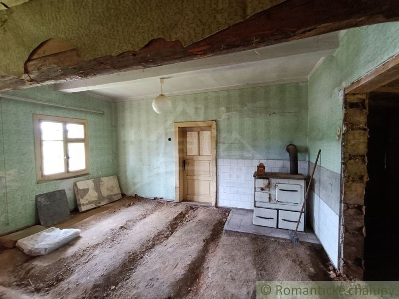 Pozemok s drevenicou na Kysuciach s krásnym výhľadom, Olešná - Interiér chaty s pecou, odkrytá podlaha, zelené steny a závesná lampa.