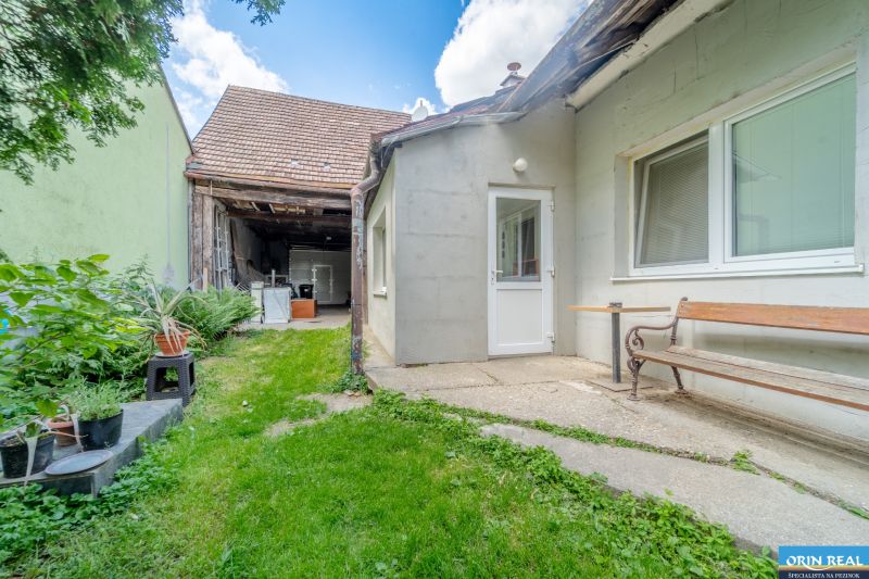 Častá RD s čiastočnou rekonštrukciou a veľkým pozemkom 2934m2 - Dvor rodinného domu na Hlavnej ulici v Častej, trávnik, lavička a rastliny.