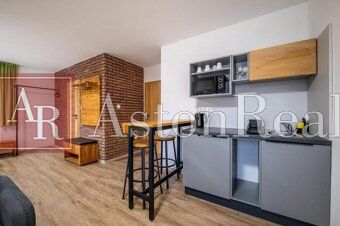 Predaj! Rekreačný apartmán pod Tatrami – Dovalovo - Interiér 1-izbového bytu s podlahou s dreveným dekorom a tehlovou stenou.