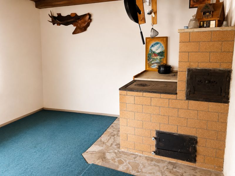 Menší Rodinný dom Veľké Košecké Podhradie, pozemok 340 m2 - Kachľová pec v rohu rodinného domu s keramickou dlažbou a obrazom na stene.