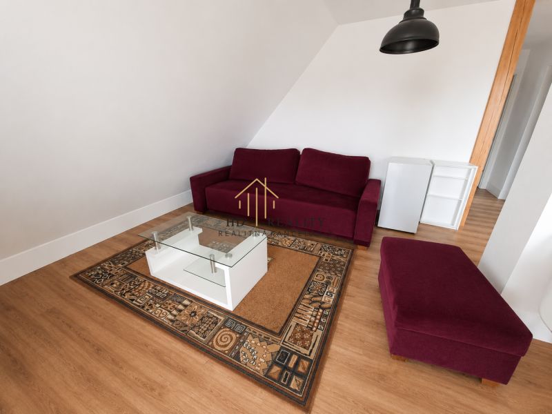 Prenájom, Apartmán v meste Krupina - Obývačka s červenou sedačkou, stolíkom na koberci a podlahou s dreveným dekorom.