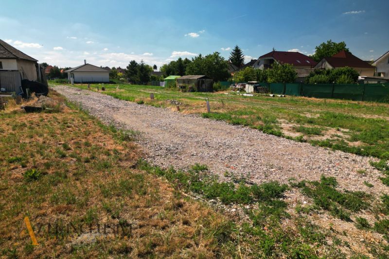 Projekt ČEREŠŇOVÁ ALEJ – 10 rod. domov/pozemk., Jelka - Pozemok pri rodinných domoch v Jelke s kamenistou cestou a zeleňou okolo.