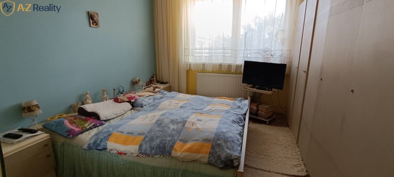 NA PREDAJ – DOM, KDE KAŽDÝ DEŇ JE DOVOLENKA - Spálňa v rodinnom dome s posteľou, skriňou, modrou stenou a televíziou.