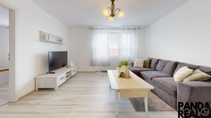  PRENÁJOM 2-izbový byt, centrum mesta s vlastným parkovaním, Topoľčany - Obývačka v 2-izbovom byte so sedačkou, TV a podlahou s dreveným dekorom.