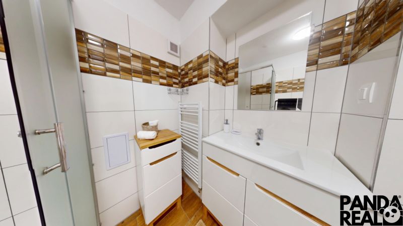  PRENÁJOM 2-izbový byt, centrum mesta s vlastným parkovaním, Topoľčany - Kúpeľňa v 2-izbovom byte s bielym nábytkom, zrkadlom a podlahou s dreveným dekorom.