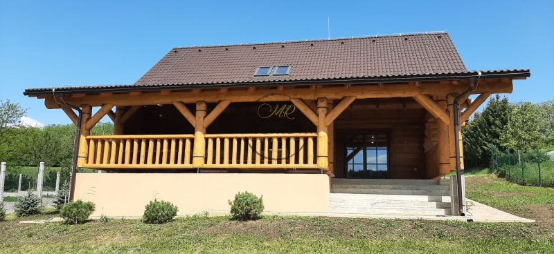 Výnimočná zrubová chata na predaj, Čechy, okr. Nové Zámky - Drevená chata na ulici v Čechách s verandou a zelenou záhradou.