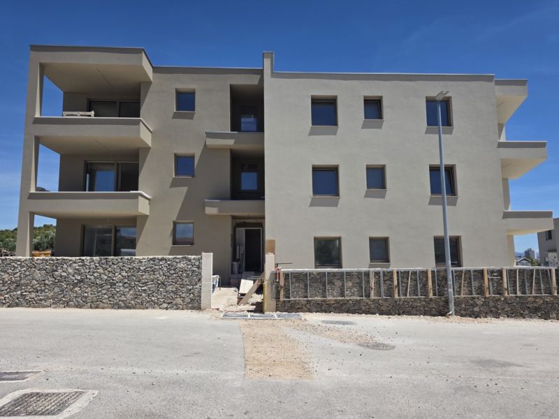 CHORVÁTSKO  - Apartmány (K2) v krásnej dedinke TRIBUNJ - Budova so 4-izbovými bytmi v Tribunji má strohú fasádu a kamenný plot.