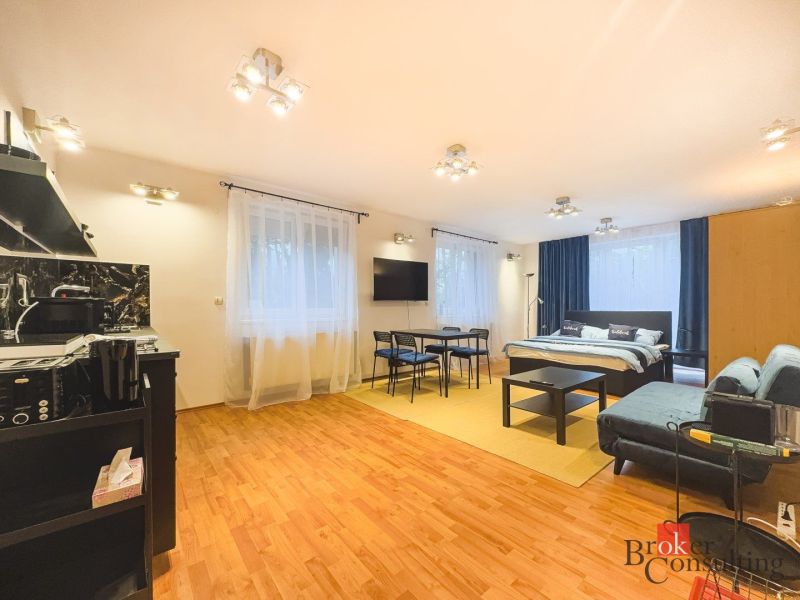 Zariadený 1i apartmán s balkónom na Hradnom kopci - Svetlý 1-izbový byt s podlahou s dreveným dekorom, posteľou, sedačkou a kuchynským kútom.