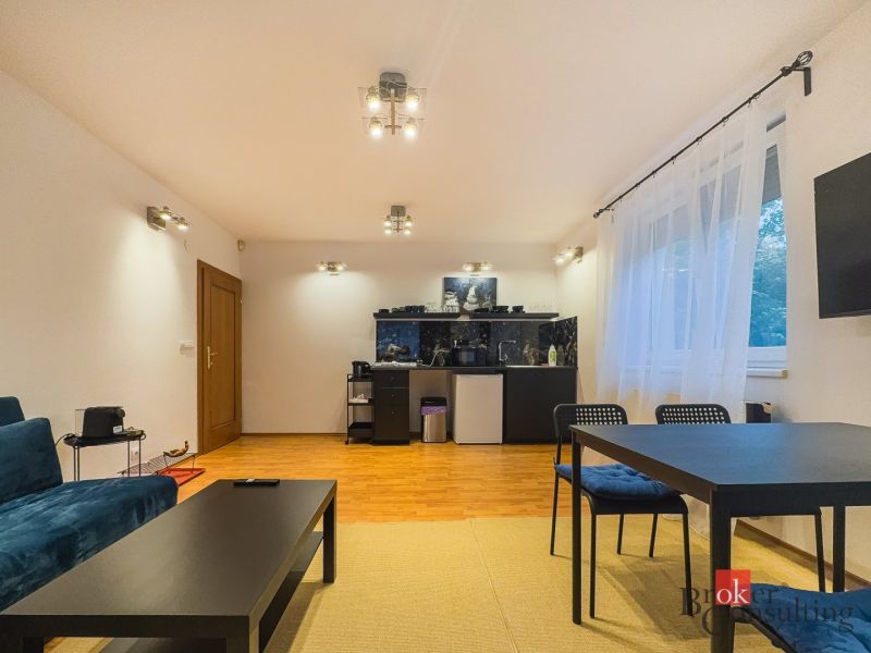 Zariadený 1i apartmán s balkónom na Hradnom kopci - 1-izbový byt s podlahou s dreveným dekorom, sedačkou, stolom a presvetlenými stenami.