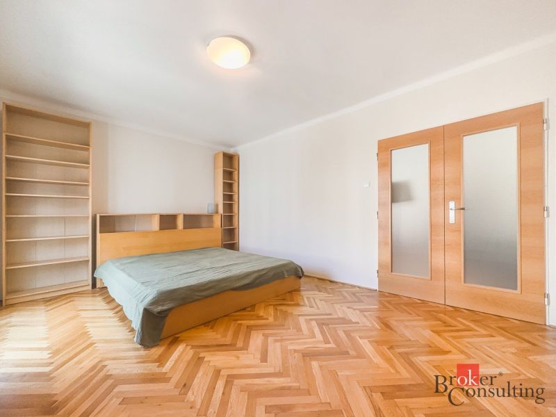 Staromestský 2i byt s balkónom na Palisádach - Spálňa v 2-izbovom byte s posteľou, knihovňami a podlahou s dreveným dekorom.