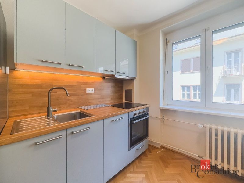 Staromestský 2i byt s balkónom na Palisádach - Kuchyňa v 2-izbovom byte s podlahou s dreveným dekorom a zabudovanými spotrebičmi.