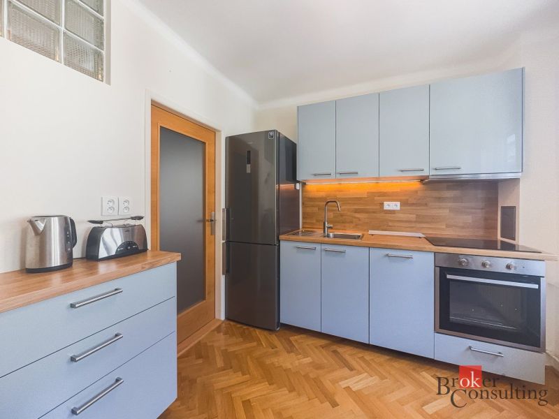Staromestský 2i byt s balkónom na Palisádach - Kuchyňa v 2-izbovom byte s podlahou s dreveným dekorom a bielymi skrinkami.
