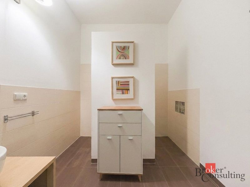 Priestranný petfriendly 2i byt v Starom Meste - Kúpeľňa v 2-izbovom byte s hnedou dlažbou, skrinkou a abstraktnými obrazmi.