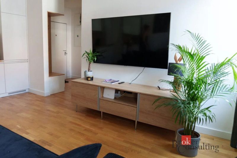 Moderný 2i apartmán v novostavbe v Starom Meste - Obývacia izba v 2-izbovom byte s podlahou s dreveným dekorom, televízorom a rastlinami.