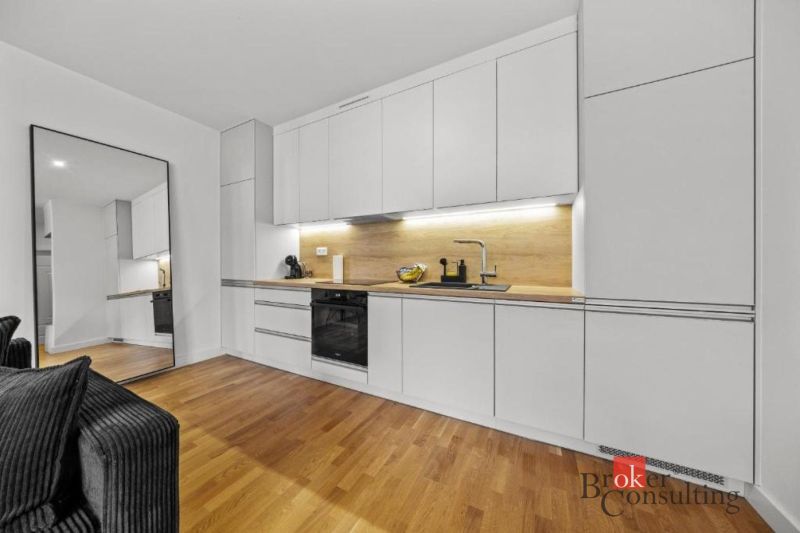 Moderný 2i apartmán v novostavbe v Starom Meste - Svetlá kuchyňa v 2-izbovom byte s bielymi skrinkami a podlahou s dreveným dekorom.