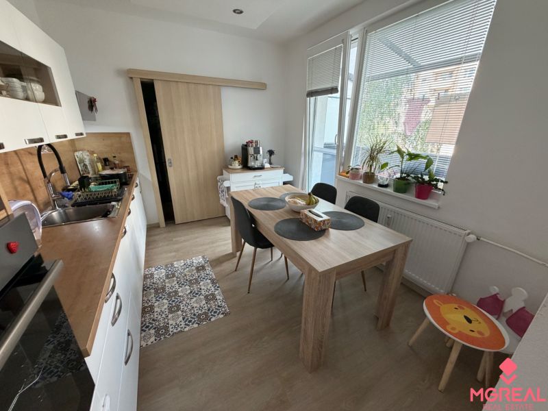 3 izbový byt s balkónom Topoľčany  - Kuchyňa v 3-izbovom byte s podlahou s dreveným dekorom a jedálenským stolom.