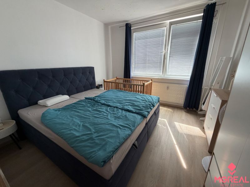 3 izbový byt s balkónom Topoľčany  - Spálňa s posteľou, detskou postieľkou a podlahou s dreveným dekorom v 3-izbovom byte.