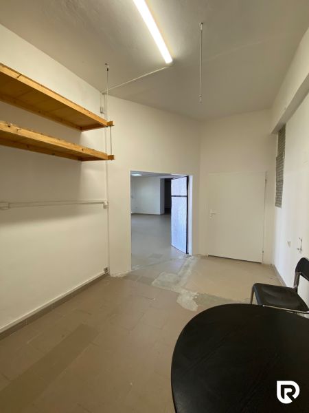 Prenájom 148,25 m² showroom, predajňa | Zlatovce - Obchodné priestory s policami, stolom a stoličkami, biele steny a jednoduché osvetlenie.