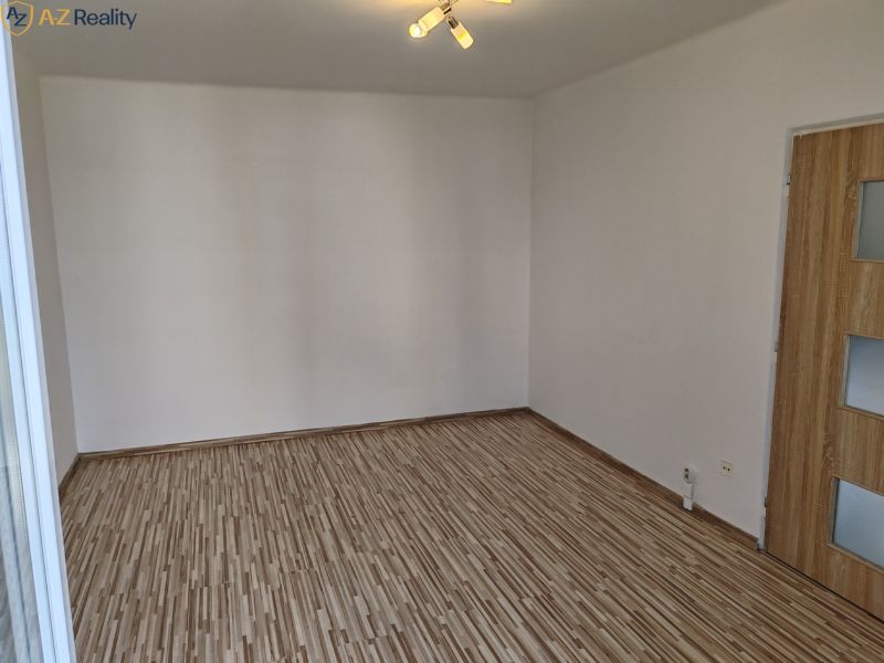 1 izbový byt s balkónom na prenájom  - Prázdna miestnosť s bielymi stenami, podlaha s dreveným dekorom, dvere so sklenenými panelmi.