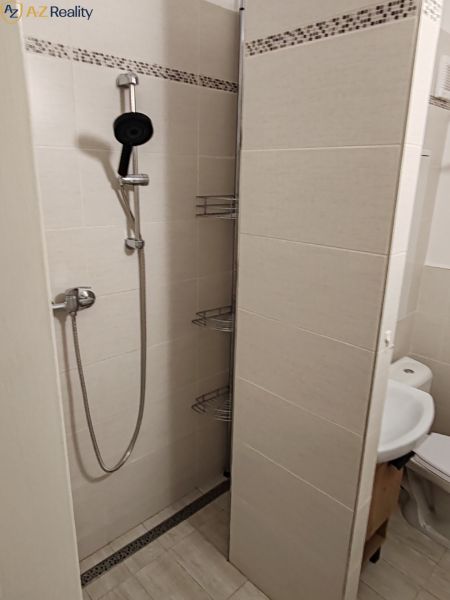 1 izbový byt s balkónom na prenájom  - Sprchový kút v kúpeľni 1-izbového bytu s bielymi obkladmi a sprchovou hlavicou.