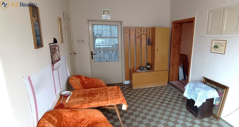 Na predaj starší rodinný dom v meste Nesvady - Obývacia izba v rodinnom dome s maľbami a čalúneným nábytkom, podlaha s kachličkami.