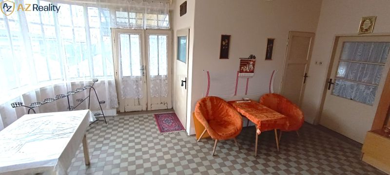 Na predaj starší rodinný dom v meste Nesvady - Interiér rodinného domu s oranžovými kreslami, stolom a bielymi záclonami.