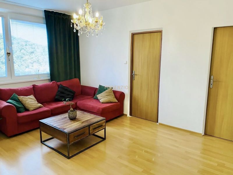 Prenajom 2,5-izbový byt v Karlovej Vsi – 48 m², výhľad do Líščieho - Obývačka v 2-izbovom byte s červenou sedačkou, luster a podlaha s dreveným dekorom.