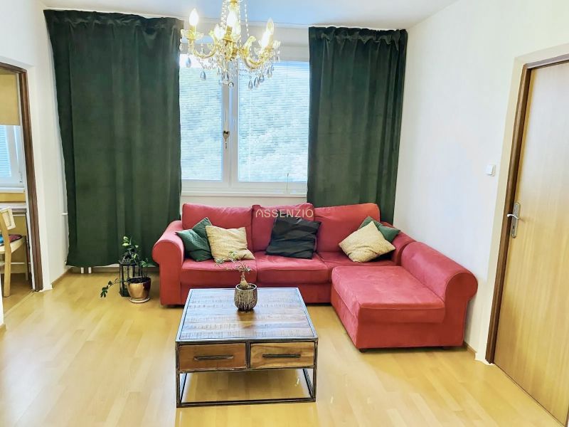 Prenajom 2,5-izbový byt v Karlovej Vsi – 48 m², výhľad do Líščieho - Obývacia izba v 2-izbovom byte s červenou pohovkou, stolíkom a závesmi.