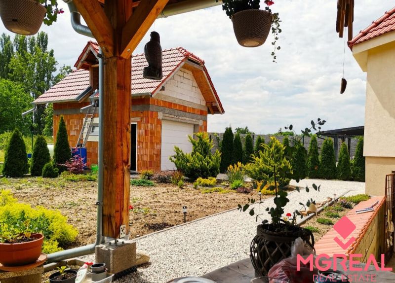 6 - izbový rodinný dom v obci Ratkovce, novostavba - Upravená záhrada a garáž pri rodinnom dome v Ratkovciach, obklopené zeleňou a drevom.