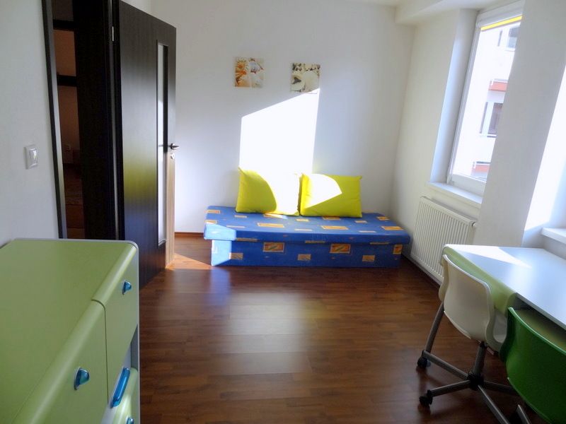 PRENÁJOM: SLNEČNÝ 3 IZBOVÝ BYT S BALKÓNOM A PARKOVANÍM, CENTRUM - Izba s podlahou s dreveným dekorom, pohovkou, stolom a sviežimi farbami v 3-izbovom byte.