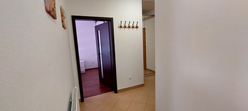 PRENÁJOM: SLNEČNÝ 3 IZBOVÝ BYT S BALKÓNOM A PARKOVANÍM, CENTRUM - Chodba v 3-izbovom byte s vešiakovou stenou a dverami s pohľadom na podlahu s dekorom dreva.