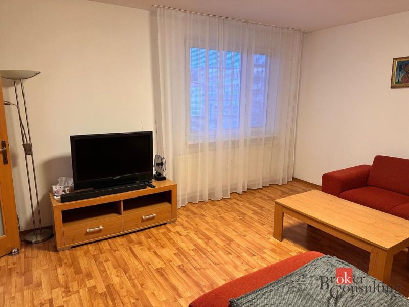 3-izbový byt Prešov, sídl. Sekčov -  REZERVOVANÉ - Obývacia izba 3-izbového bytu s podlahou s dreveným dekorom, TV a červeným sedením.